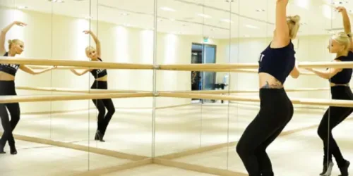 Femeie exersand la o sedinta specifică de Barre, privindu-se in oglinda